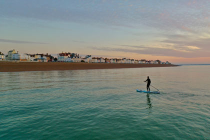 A person on a paddleboard on a calm sea with Deal seafront and beach in the background.