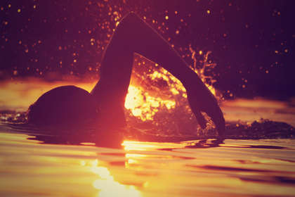 Sea swimmer in golden sea at sunrise.