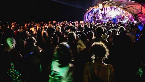 A crowd in front of an outdoor stage lit up at night.