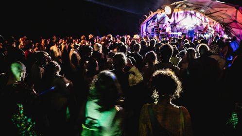 A crowd in front of an outdoor stage lit up at night.