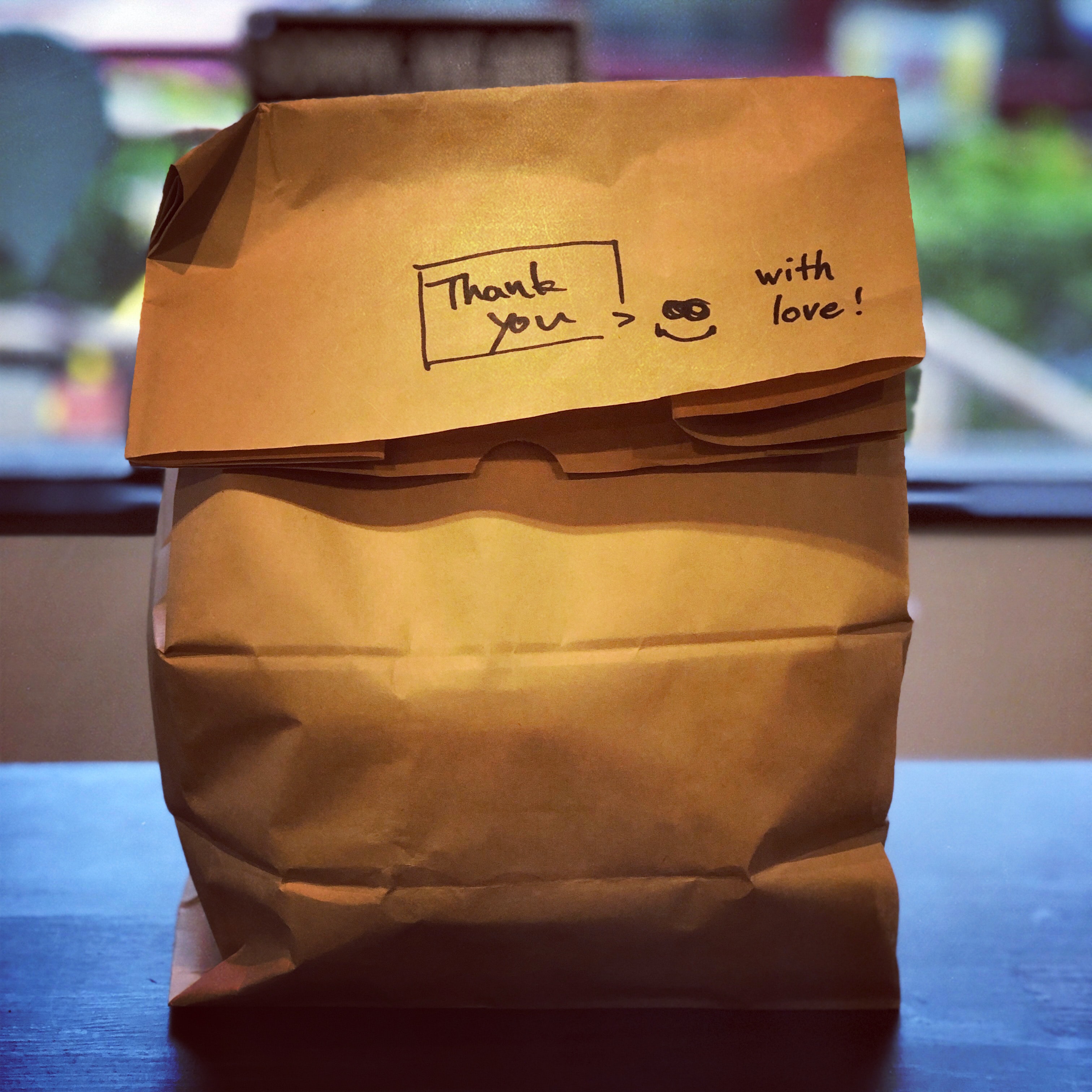 A brown paper takeaway back with the words 'Thank you - with love' written on.