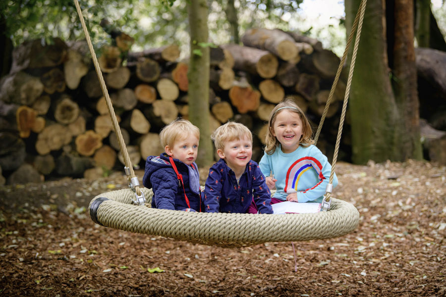 Three children in a large swing seat with logpile behind
