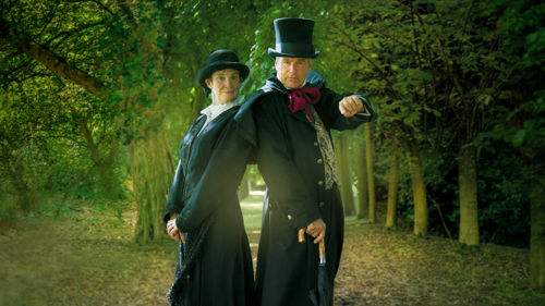 A couple dressed in black Victorian clothing in a spooky woodland scene