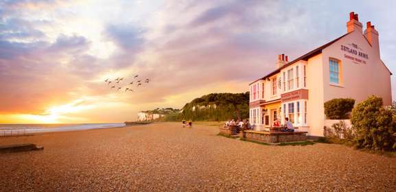 The Zetland Arms located on a pebble beach with cliffs in the background.