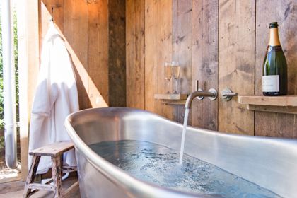 A metal bathtub filling up with water in a wood-panelled room.
