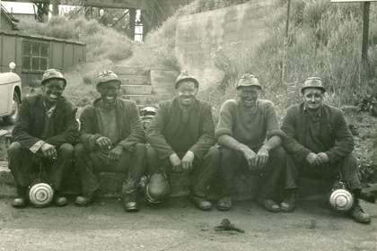 A sepia photograph of 5 miners above ground.