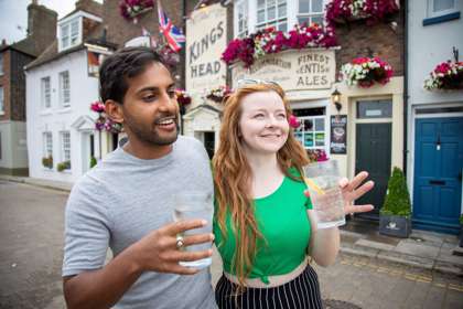 A man and a woman holding glasses in front of a pub