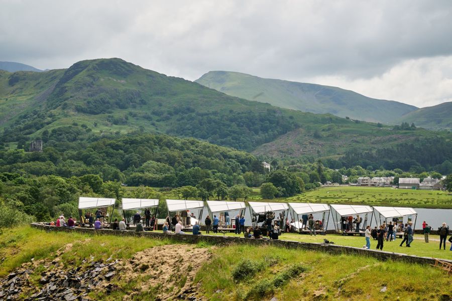 A line of artists in shelters in a hilly landscape