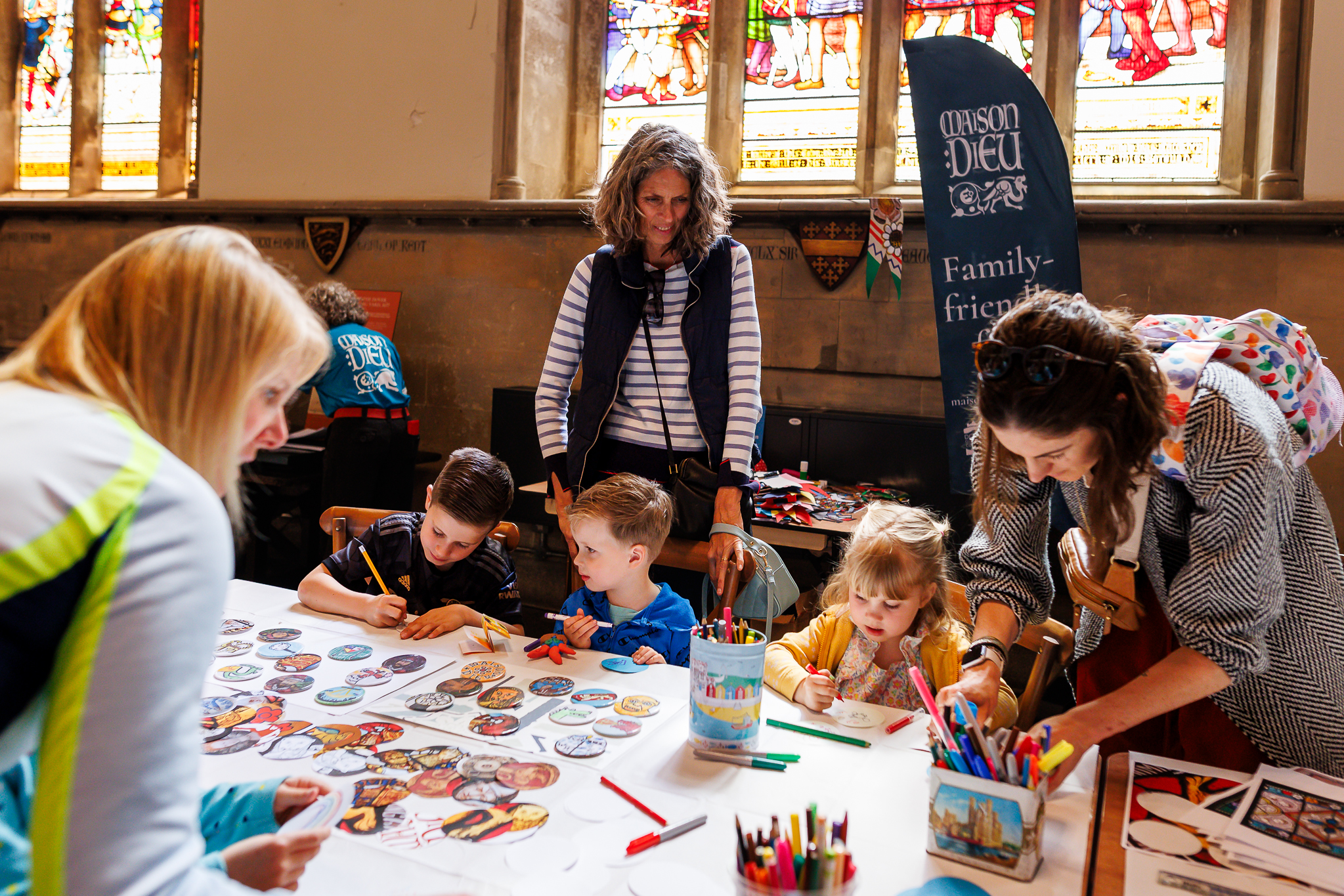 Children creating badges, adults looking on, stained glass behind