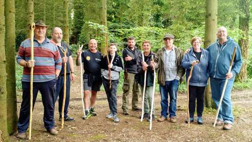 A group of nine men and women in the woods with handmade walking staffs