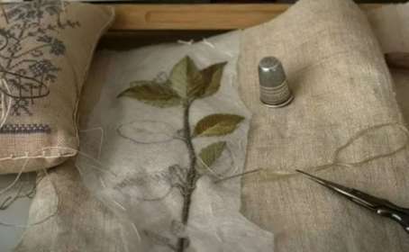 Piece of embroidered material with leaf design next to a thimble and scissors
