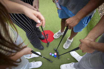 Looking down at four golf balls and clubs and four pairs of feet standing in a circle.