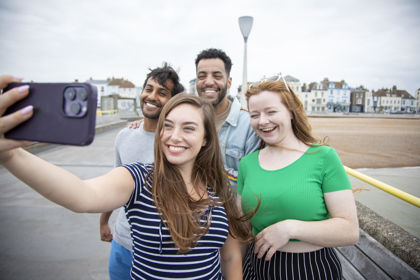 A group of four young people taking a selfie on Deal Pier with the town and seafront in the background