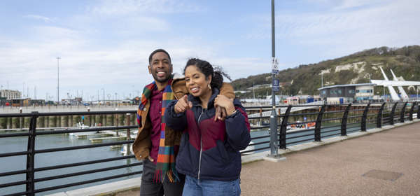 Two people walking along Dover pier with the marina in the background. 