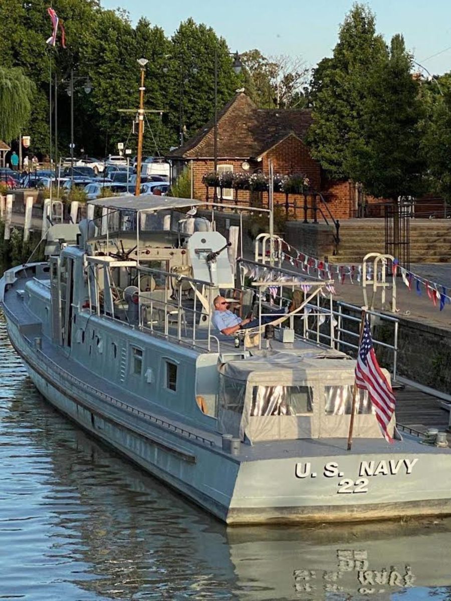 The grey 80-ft US Navy patrol boat on the River Stour moored at Sandwich Quay next to a wooden pontoon.
