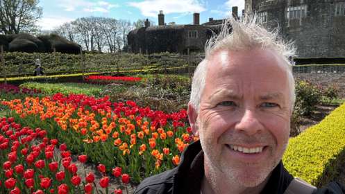 A man standing in front of rows of red and orange tulips