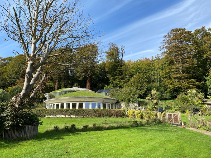 A low round building with green roof in a garden setting