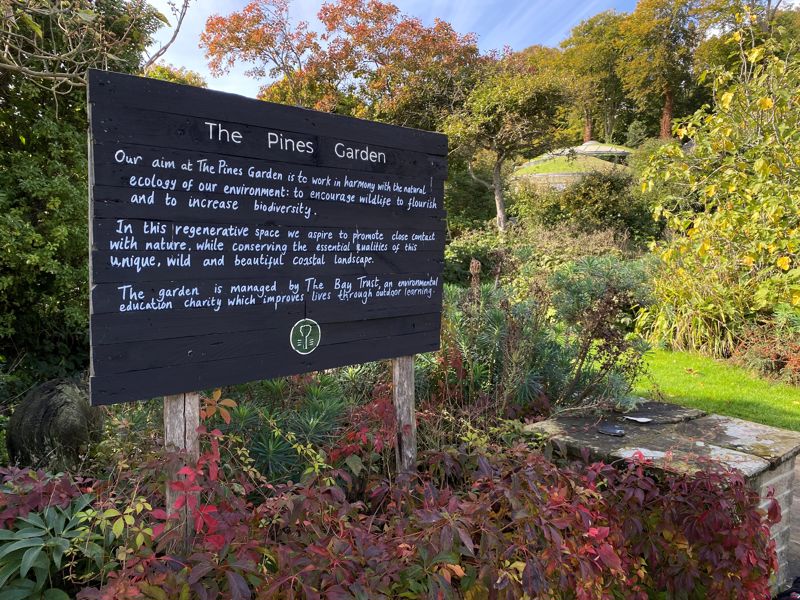 An information sign at the entrance to the gardens with autumnal leaves in the foreground.