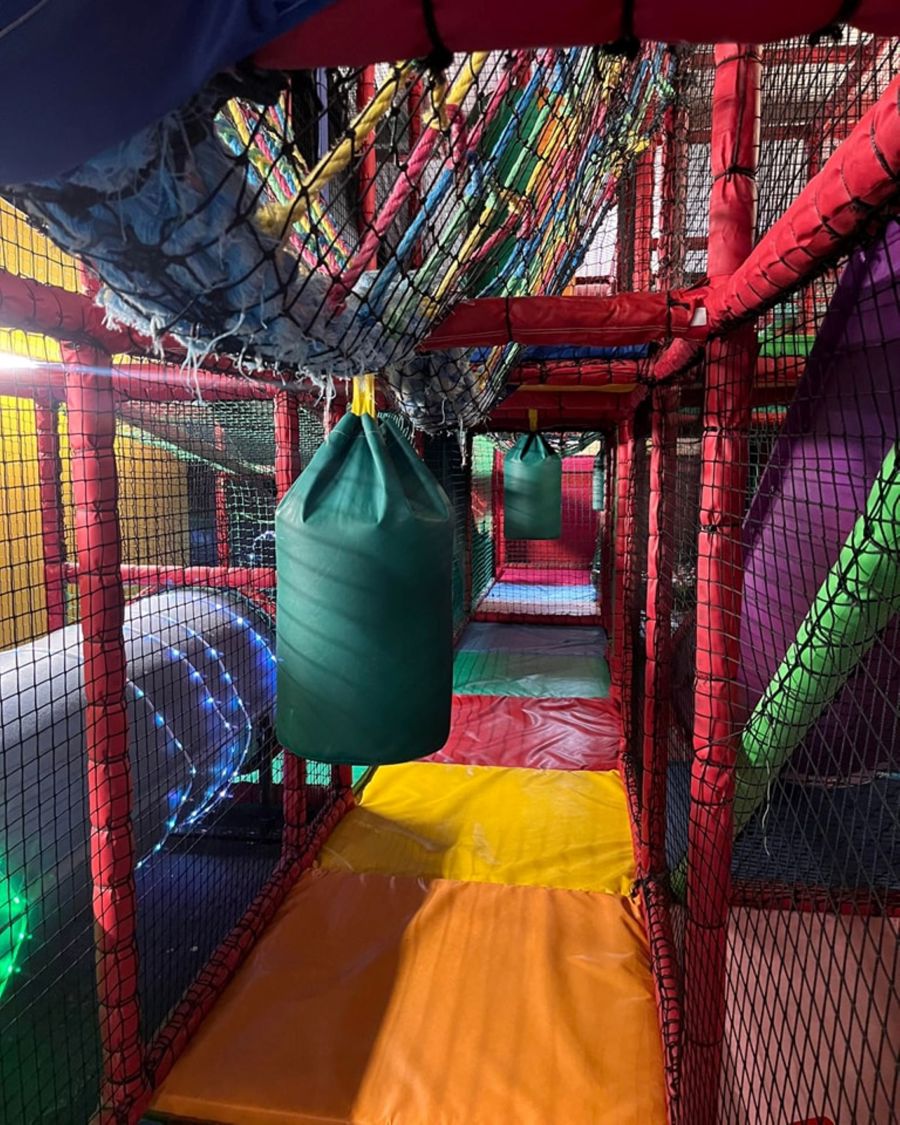 A colourful indoor soft play area with mats, tunnels and punch bag.