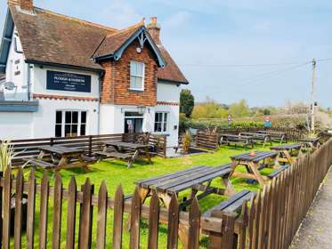 Exterior of The Plough & Harrow with tables and benches in the beer garden at the front of the pub