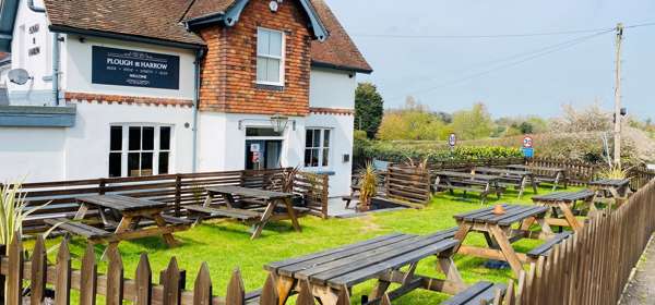 Exterior of The Plough & Harrow with tables and benches in the beer garden at the front of the pub