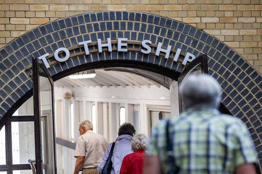 People walking towards a doorway with a 'To the ship' sign above.