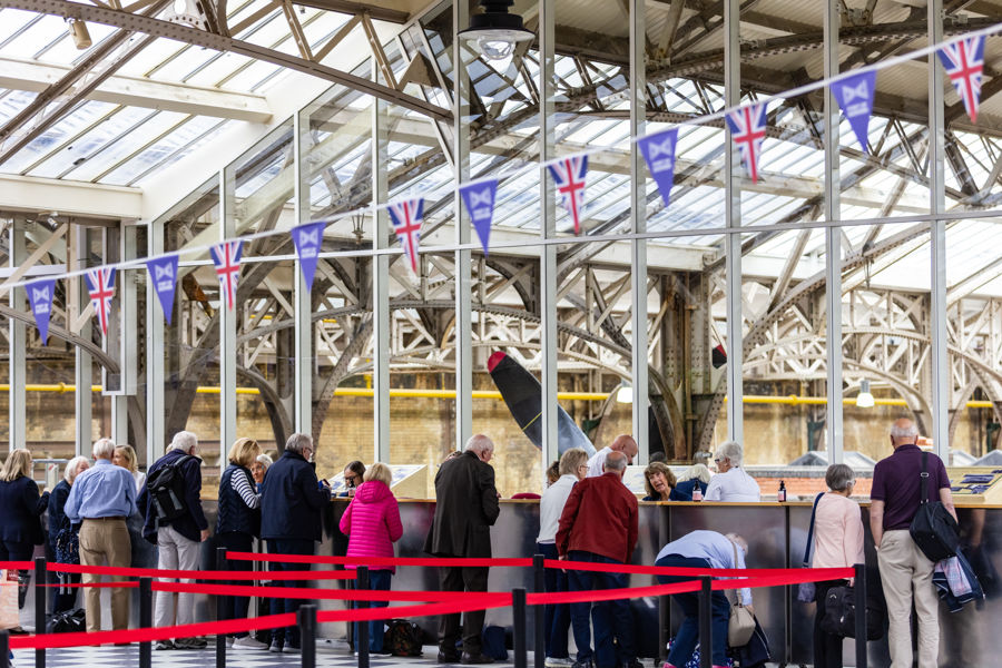 A line of people checking in at Cruise Terminal 1 with the old station architecture behind. 