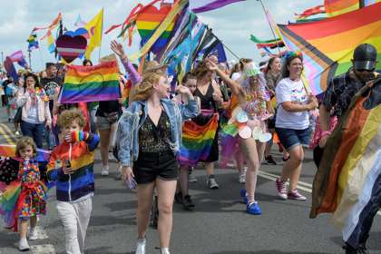 A crowd of people walking along waving rainbow flags.