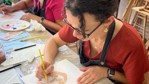 A dark-haired lady in a red t-shirt and black apron is painting a self-portrait