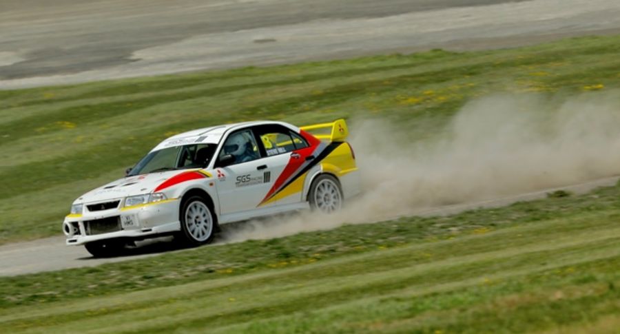 A white rally car with red, yellow & black markings racing round a track.