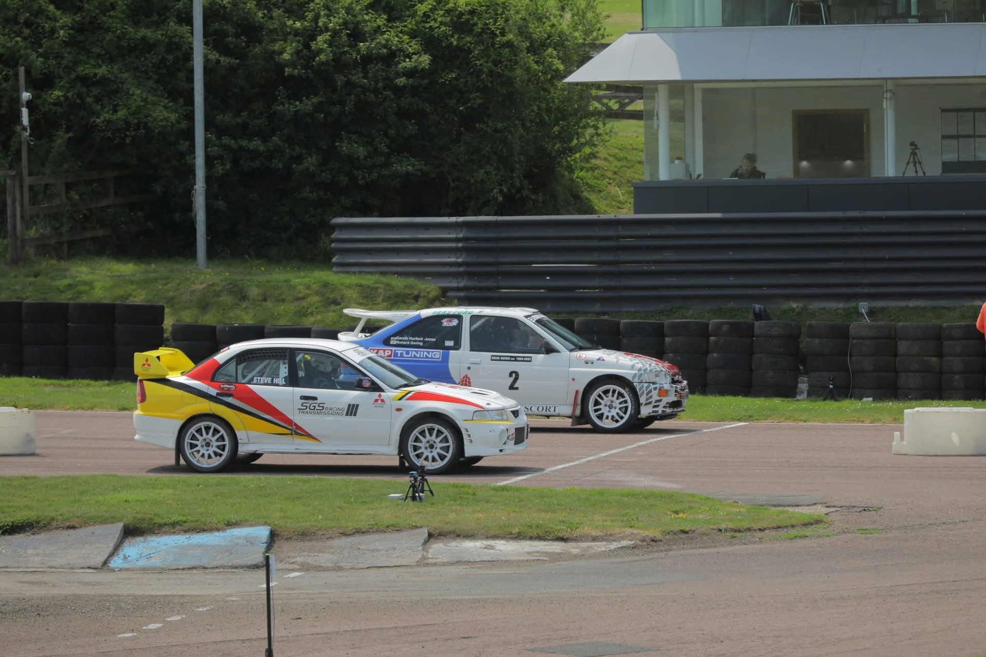 2 white racing cars waiting at a start line to race round a circuit.