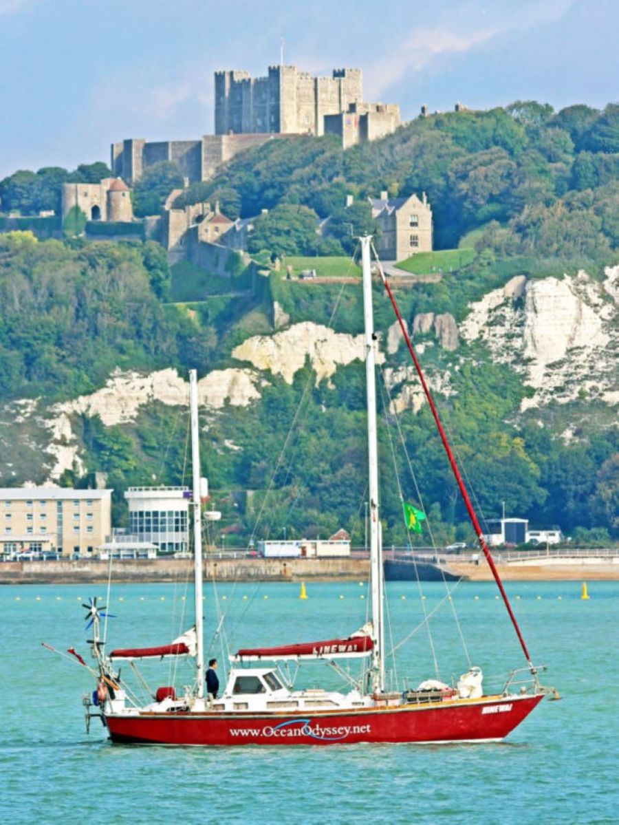 A red yacht in Dover Harbour with Dover Castle on the cliffs in the background.