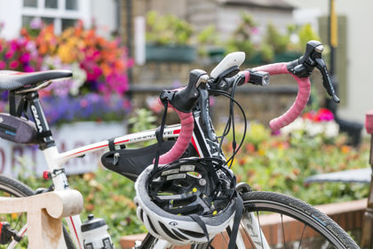 A racing bike and helmet leant against a bench with pink, orange and purple flowers in the background.