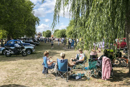 A group of people having a picnic with classic cars lined up in the background