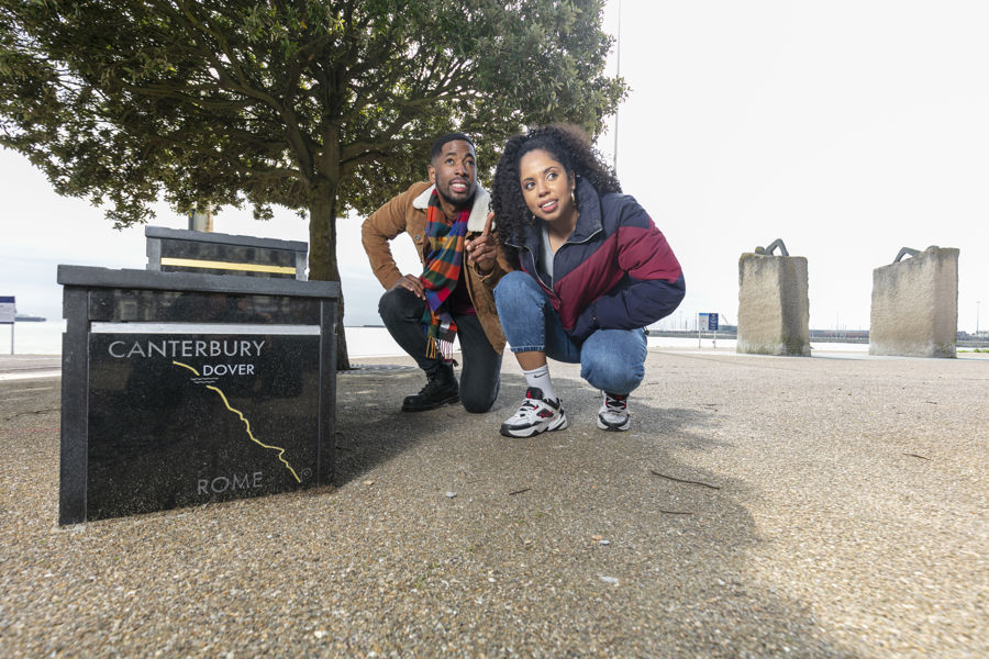 Two people beside a black granite sculpture of a winners podium on Dover seafront.
