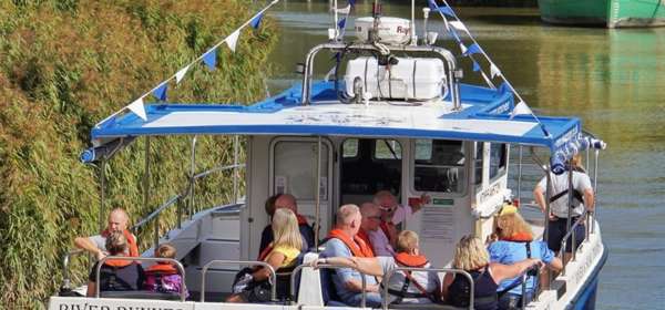 People aboard the blue and white Sandwich River Runner boat on the  River Stour heading away from the camera.
