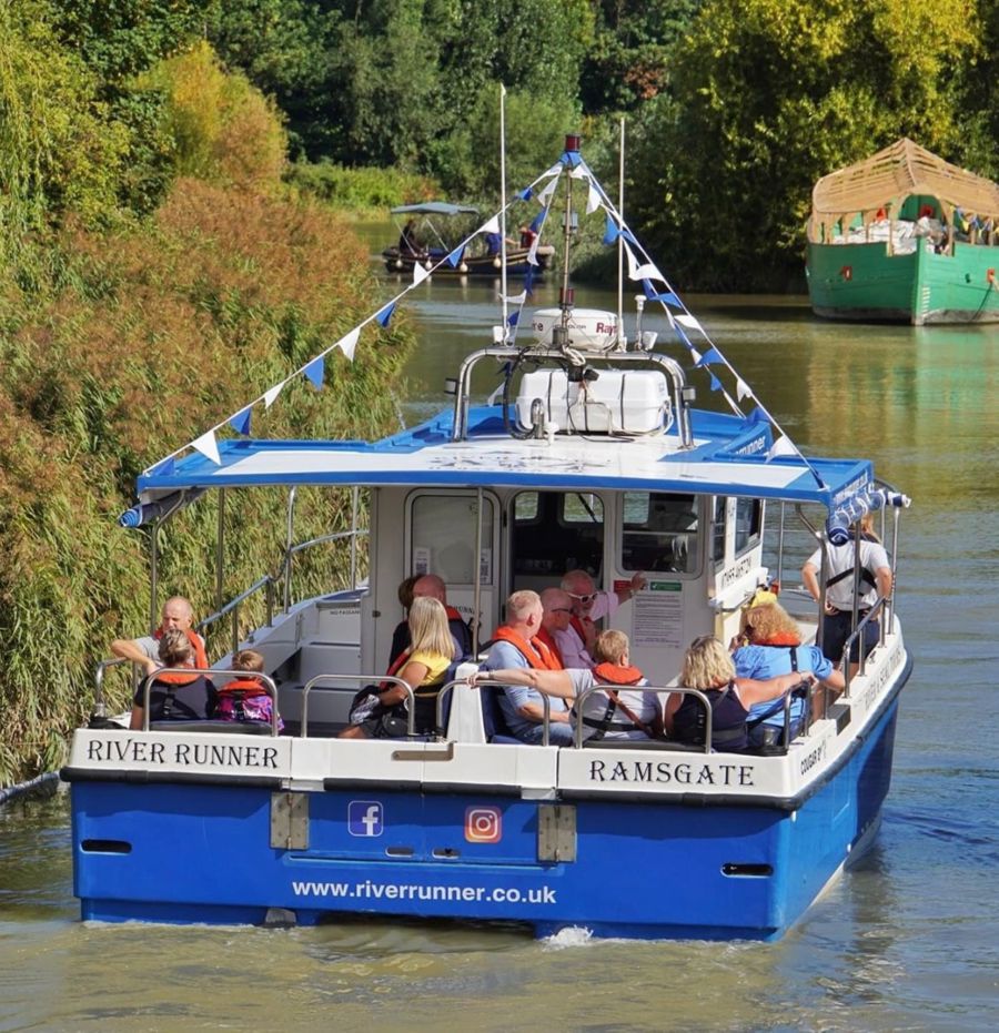 People aboard the blue and white Sandwich River Runner boat on the  River Stour heading away from the camera.