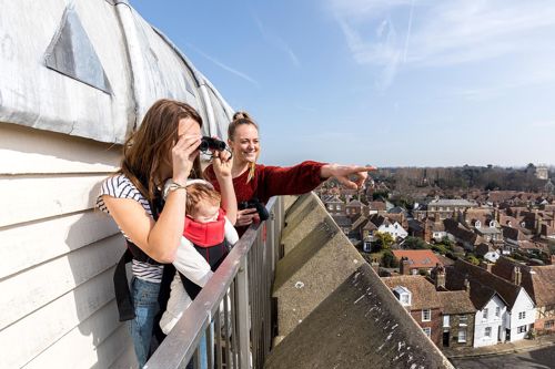 Two women, one with a baby in a papoose, at the top of St Peter's Church tower looking out over Sandwich rooftops.