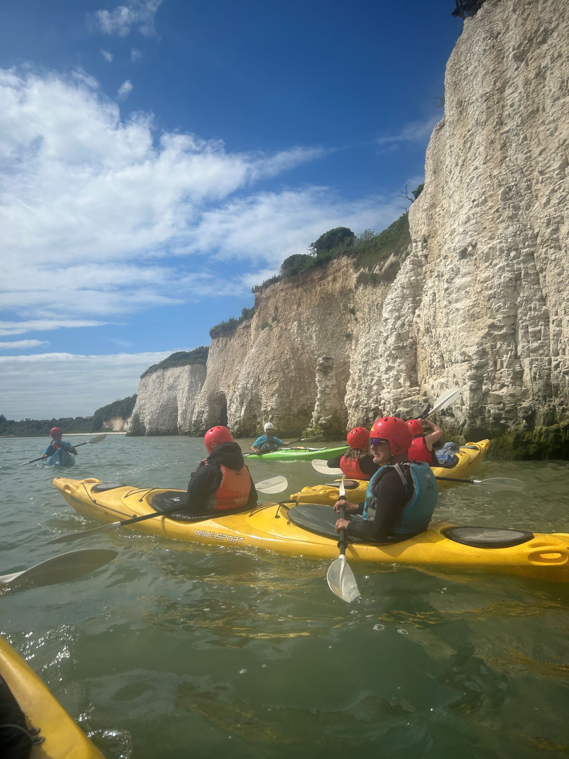 A group of people in double kayaks with the white cliffs behind