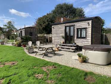 Outside view of Shepherds Huts at Spitfire Barn with seating area and hot tub