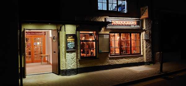 An exterior image of The Smugglers Inn at night with inviting lit doorway and windows