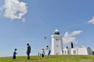 A family flikes kites outside a white Victorian lighthouse