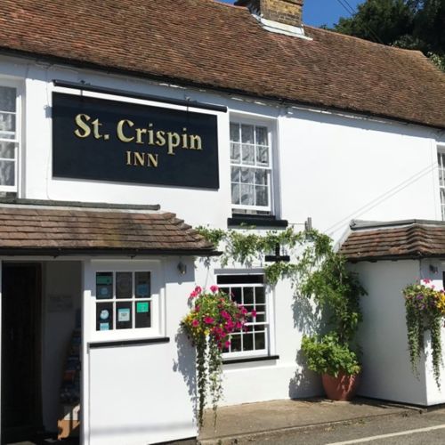 Exterior of the St Crispin Inn with whitewashed walls and colourful hanging baskets