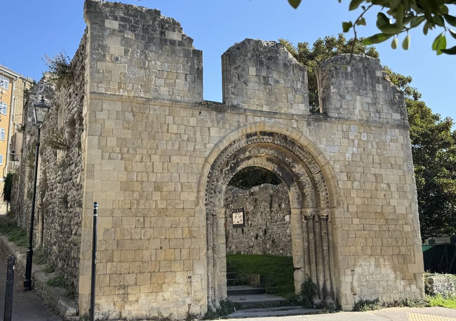 A pale stone facade of a ruined church with a Norman archway