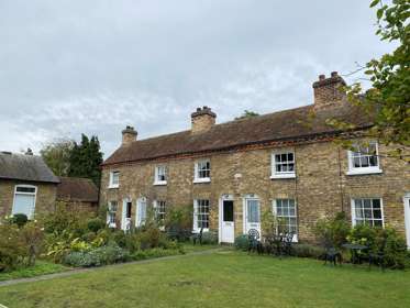 A row of sandy brick terraced cottages with gardens in front.