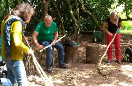Three people stripping long lengths of wood to make staffs.