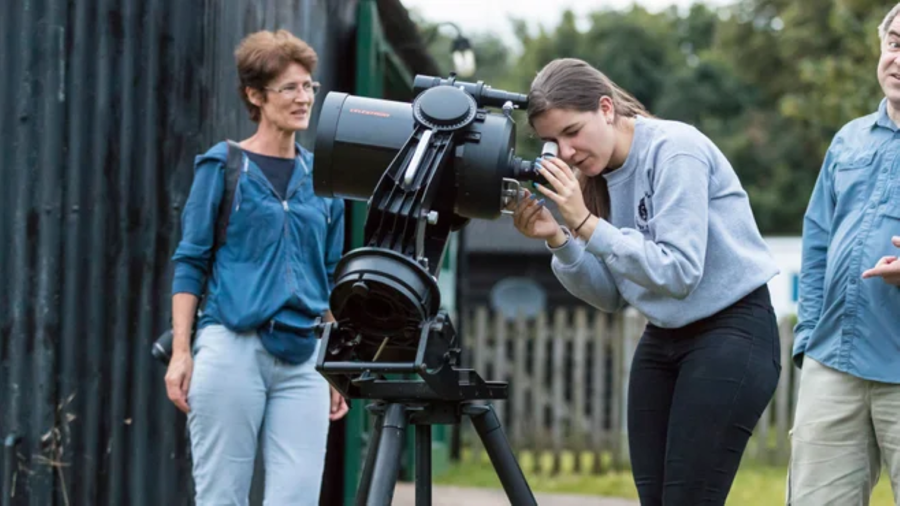 A young woman looks through a telescope