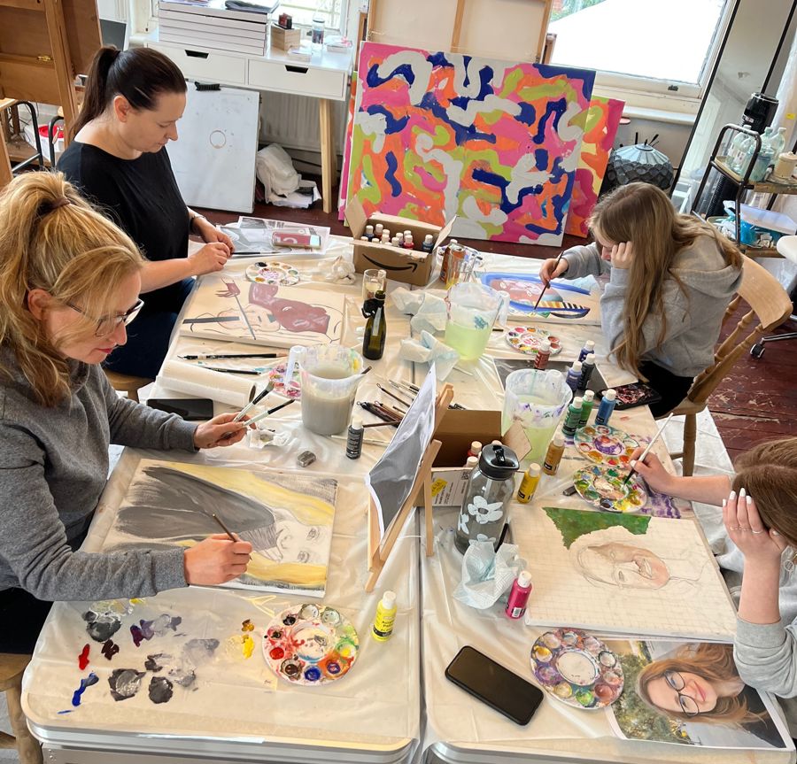A group of four people sat at a table painting with artworks around the walls.