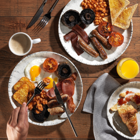 Overhead shot of two plates of full English breakfasts and a plate of croissants.