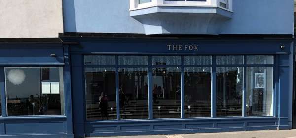 The blue-painted exterior of The Fox in Deal with large glass windows overlooking the pier.